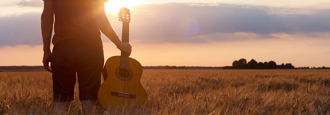 A man standing in a wheat field, holding a classical guitar