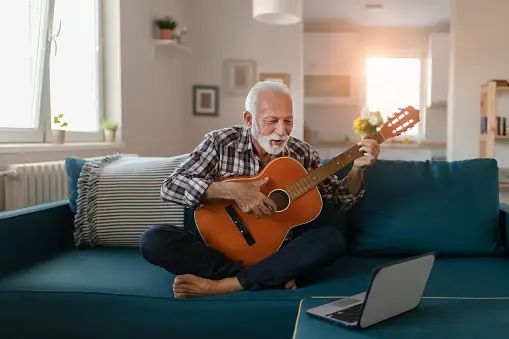 An elderly man holding a classical guitar, learning to play the guitar online.