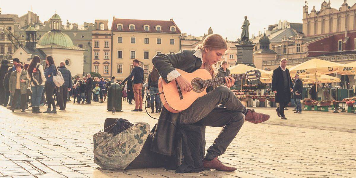 The guitarist sitting on the square and playing the guitar